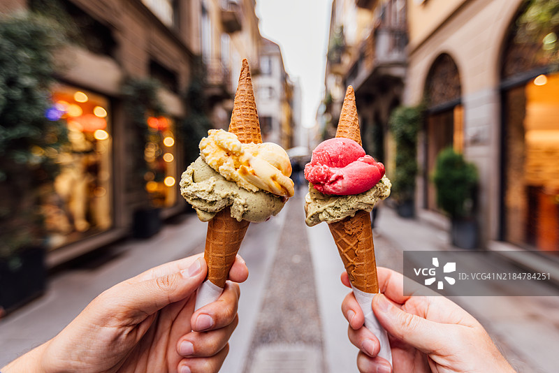 两个人在意大利伦巴第大区米兰的街道上手持五彩缤纷的冰淇淋。图片素材