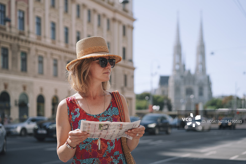 在奥地利维也纳，街上有一位女性正在阅读报纸，背景是祈祷教堂。图片素材