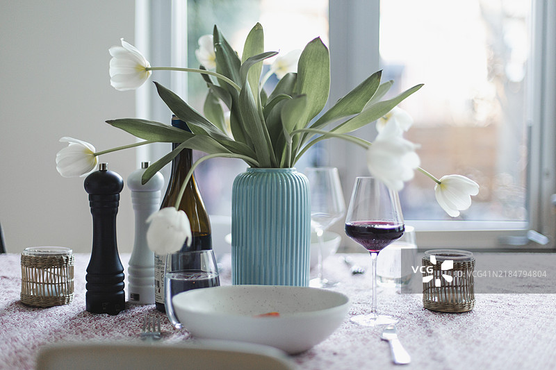餐桌上摆放着白色郁金香、餐具和一杯红酒图片素材