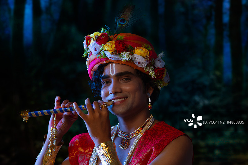 年轻男子打扮成克里希纳神，庆祝贾纳马斯塔米节，特写肖像，正在吹奏长笛。图片素材