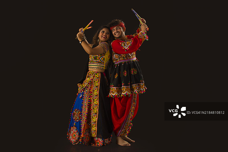 在黑色背景下，快乐的年轻情侣在纳瓦拉特里庆祝活动中表演丹迪亚拉斯舞。图片素材