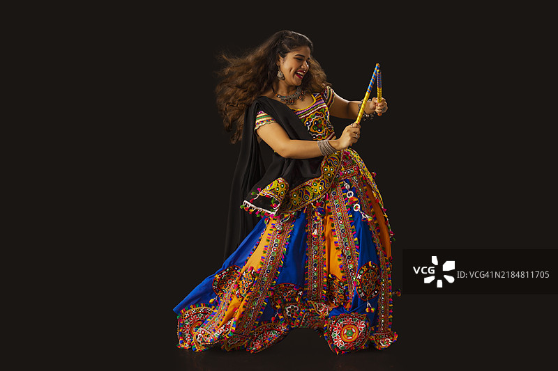古吉拉特女性在黑色背景下手持丹迪亚棍跳舞，庆祝纳瓦拉特里节。图片素材