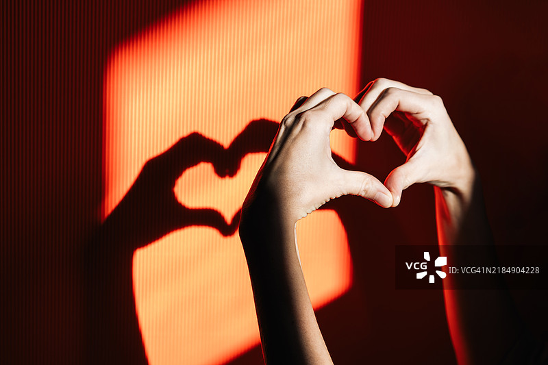 一颗由手组成的心与其在阳光明媚的黄色背景上的阴影，象征着爱。图片素材