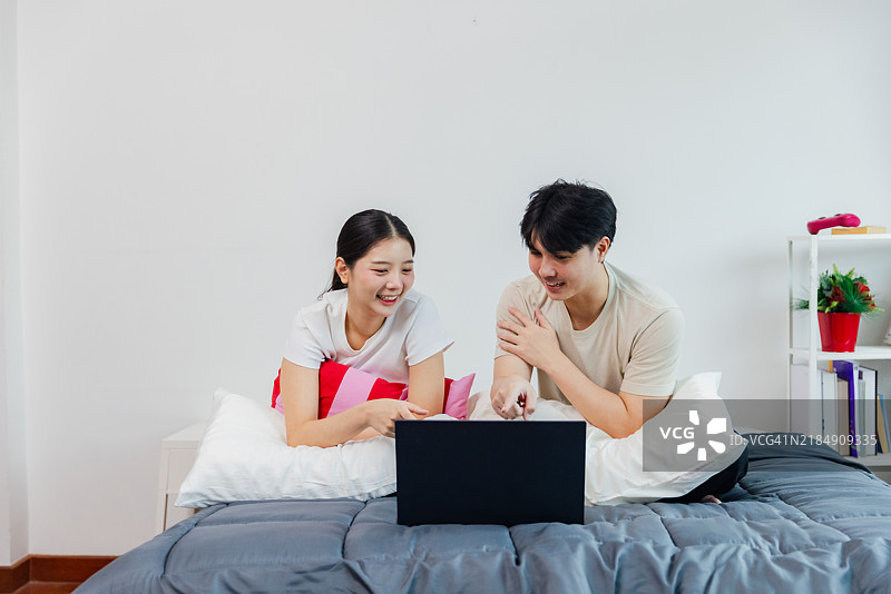 一对情侣在温馨的卧室环境中享受学习和使用笔记本电脑的美好时光。图片素材