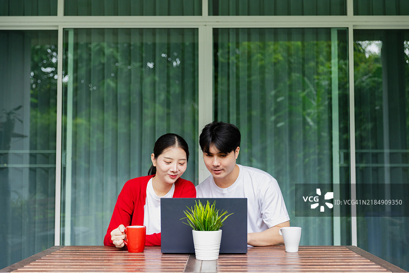 一对年轻情侣在阳光明媚的日子里，坐在户外的桌子旁一起使用笔记本电脑，享受彼此的陪伴，气氛轻松愉快。图片素材