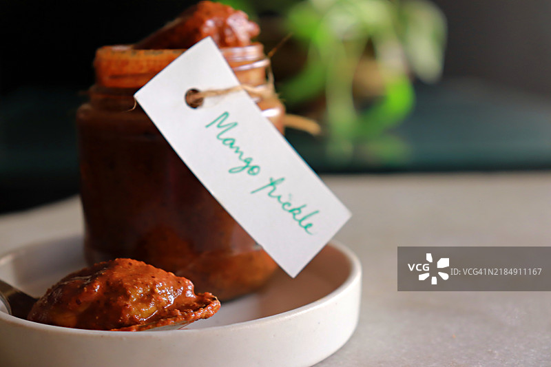 香辣嫩芒果腌菜装在玻璃梅森罐中，带有手写标签/标记 - 静物摄影图片素材