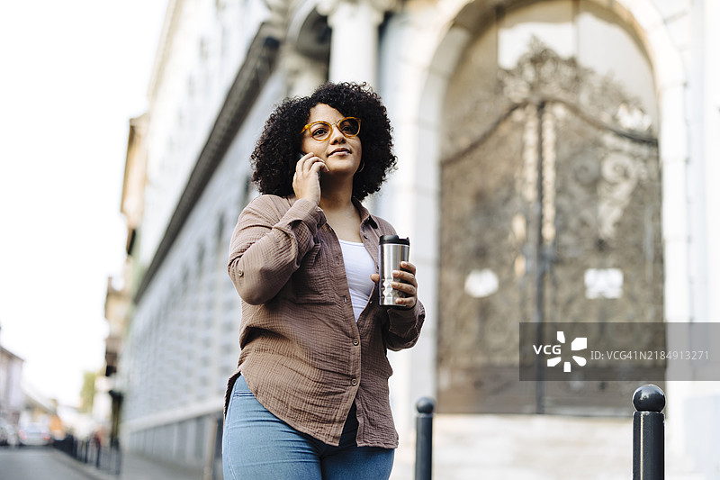 年轻的非洲裔女性在街上喝咖啡并使用智能手机图片素材