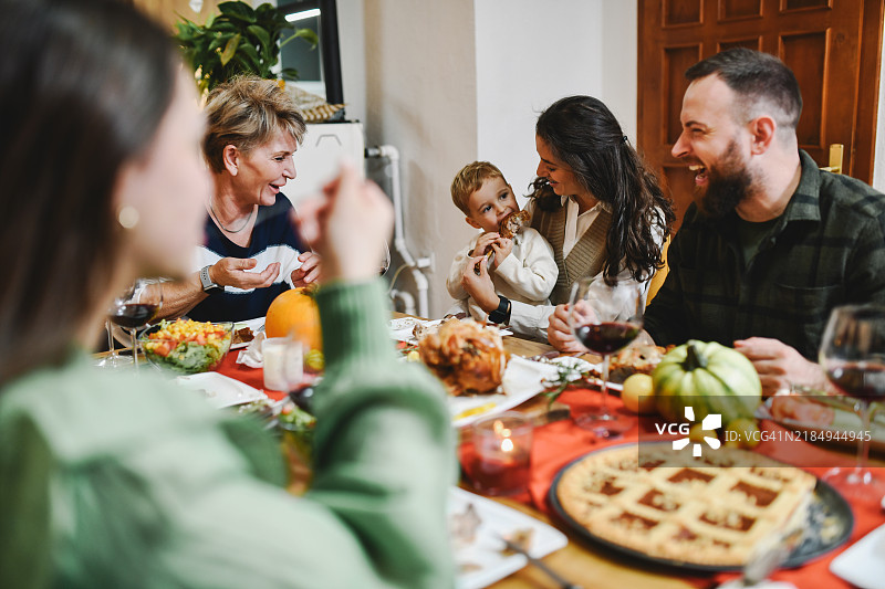 可爱的幼儿坐在母亲的腿上吃着一块火鸡肉，母亲在欣赏他。图片素材