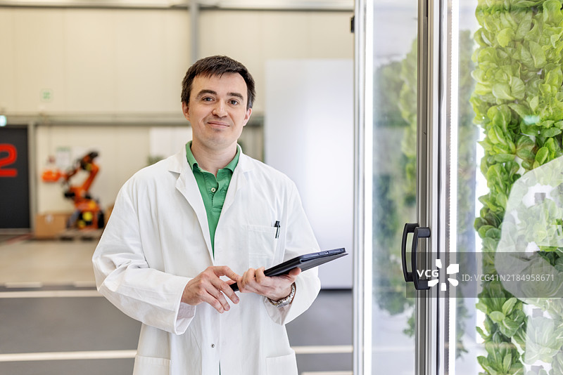 科学家手持数字平板，站在垂直农场的气雾栽培塔旁图片素材