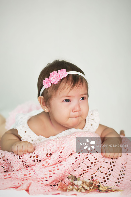 戴着粉色花朵头带的婴儿，安静地躺在粉色钩织毛毯上图片素材