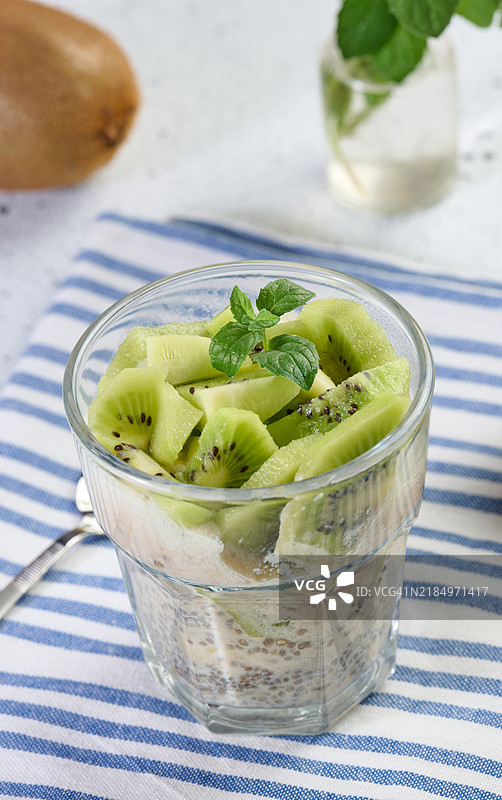 玻璃杯装的奇亚籽酸奶甜点，上面点缀着新鲜的猕猴桃片，放在白色桌子上。图片素材