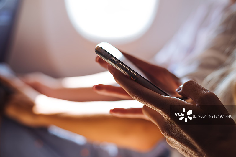 飞机上手部特写，使用智能手机，强调在空中旅行中与科技的连接。适合与机上娱乐、连接性和现代旅行相关的概念。图片素材
