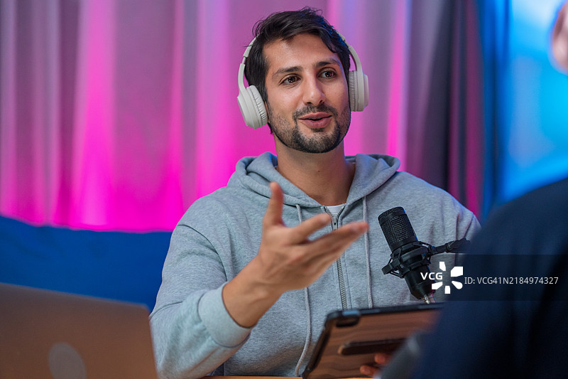 一位拉丁裔男性播客主持人在录音室与嘉宾互动，提供专业知识和有影响力的讨论，面向专业观众。图片素材