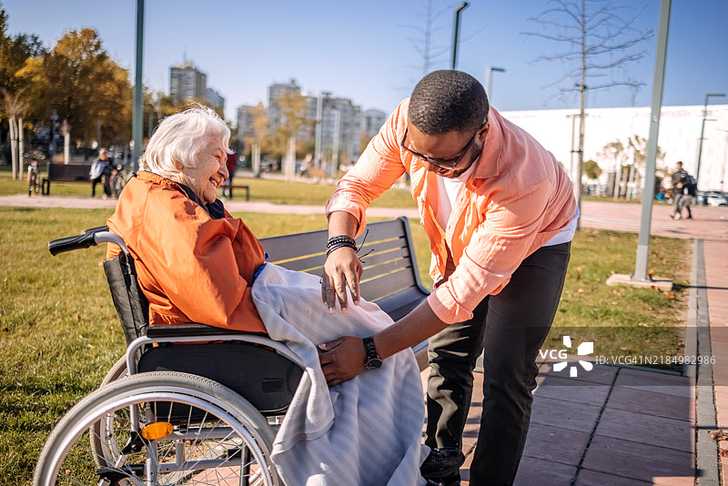 年轻志愿者在户外照顾坐在轮椅上的老人，努力用毯子为他们保暖。图片素材