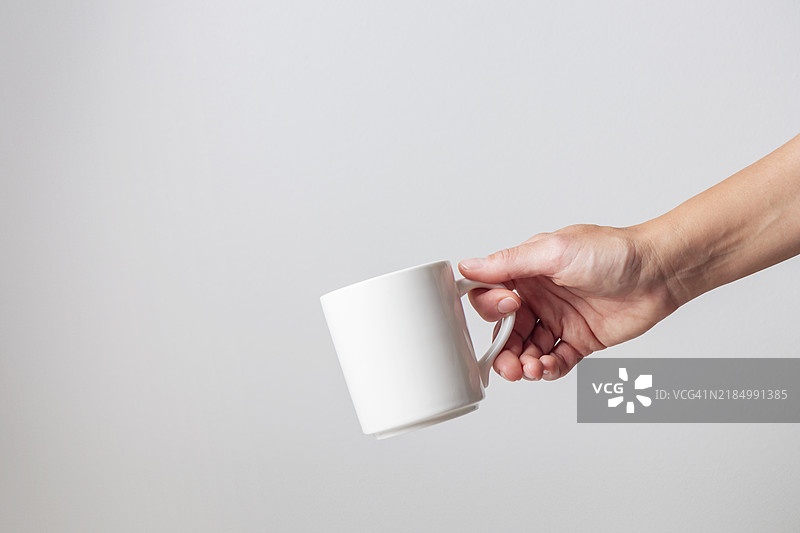 一只白色空白陶瓷杯在女性手中，背景为白色，食品样品展示图片素材