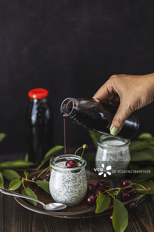 女人在乌克兰的奇亚籽布丁圣代上倒樱桃汁图片素材
