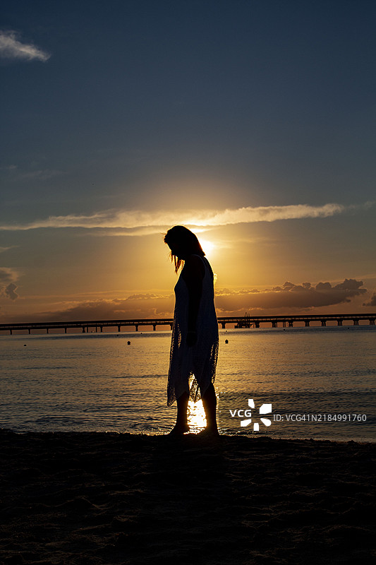 日落时分，意大利福贾曼弗雷多尼亚海滩上站着的女性剪影。图片素材