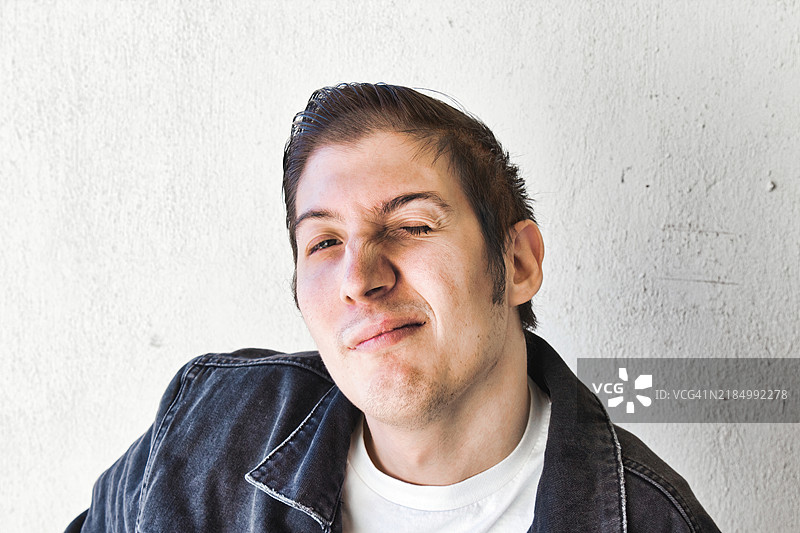 一位年轻男子的肖像，打扮成1960年代的油头，梳着向后梳的头发，穿着牛仔夹克，脸上带着调皮的表情，正直视镜头，美国，USA图片素材