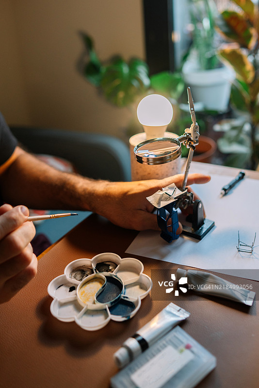 特写镜头下的男子正在使用微距工具和放大镜为微型模型车上色图片素材