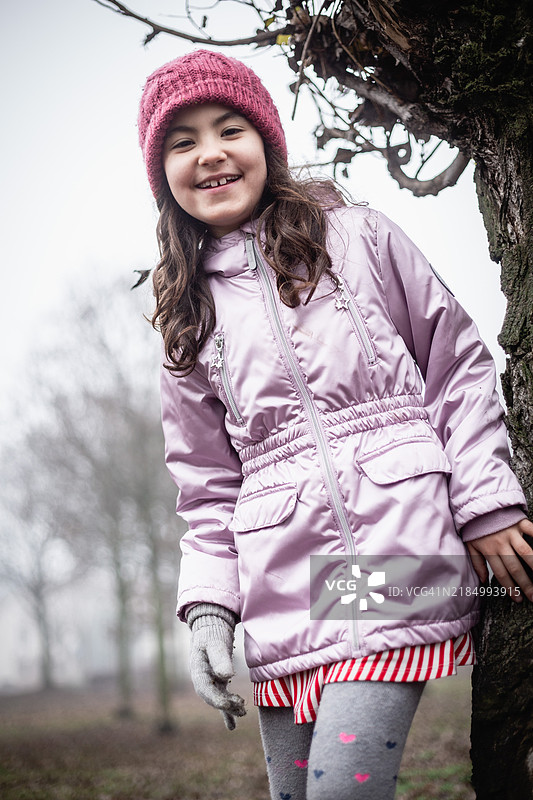 低角度视图的微笑女孩站在树旁，戴着粉色帽子图片素材