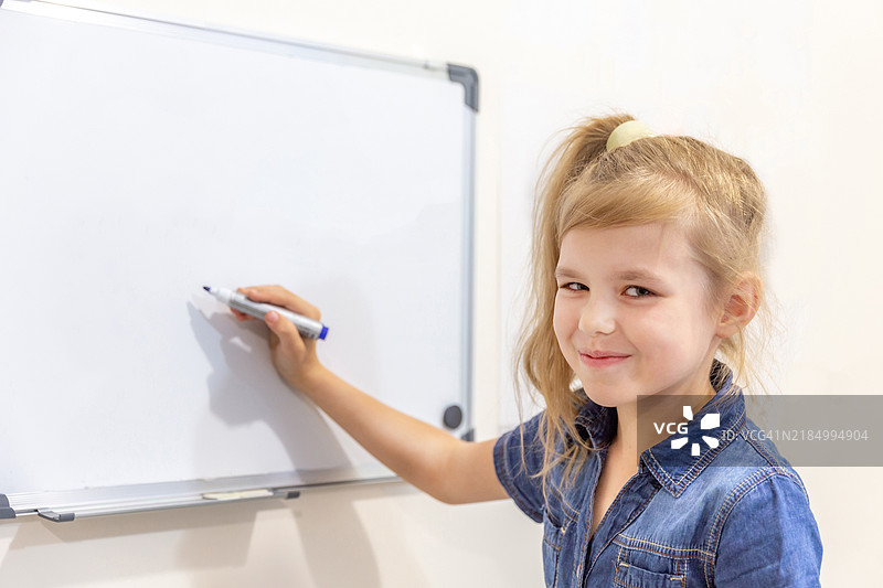 小女孩微笑着用马克笔指着空白白板图片素材