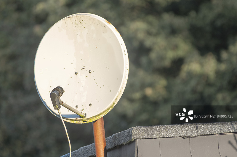 屋顶上的旧卫星天线，接收信号，背景是模糊的树木。图片素材