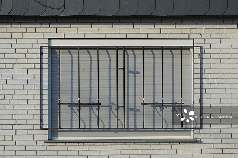白砖墙上覆盖窗户的金属栏杆，配有降下的百叶窗，提供安全性并防止入室盗窃。图片素材