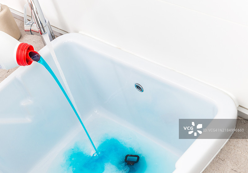 在洗衣盆前将蓝色洗涤剂倒入空水槽中图片素材