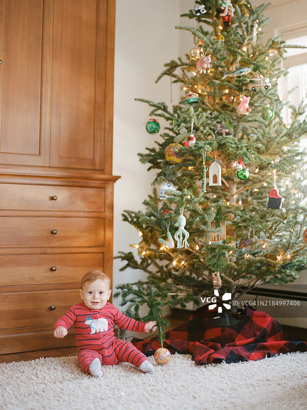 红头发的小男孩坐在装饰好的圣诞树旁，位于一个小城市的公寓里。图片素材