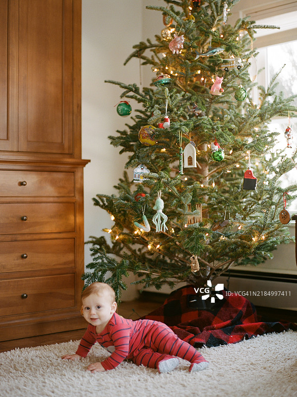 红头发的男婴侧躺在装饰好的圣诞树旁，位于一个小城市的公寓里。图片素材
