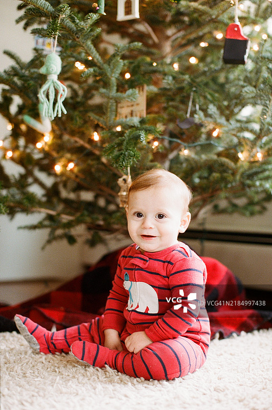 红发男婴坐在装饰好的圣诞树旁，身处一个小城市的公寓里图片素材