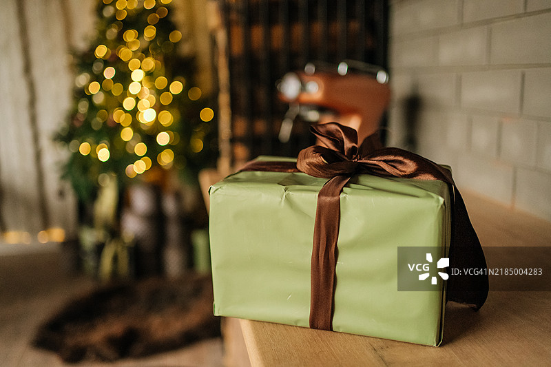 木桌上放着一个礼品盒，背景是圣诞树。图片素材
