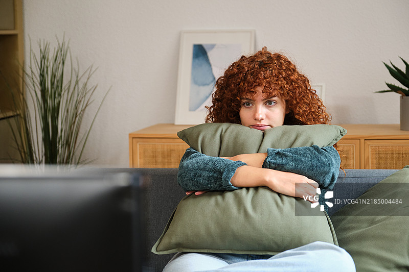 孤独的女人在家里抱着枕头看电视图片素材