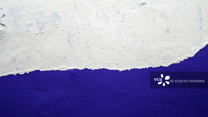 宏观摄影：一张蓝色海报粘贴并撕裂在有纹理的白色墙壁上。阳光。自然色彩。法国巴黎。图片素材