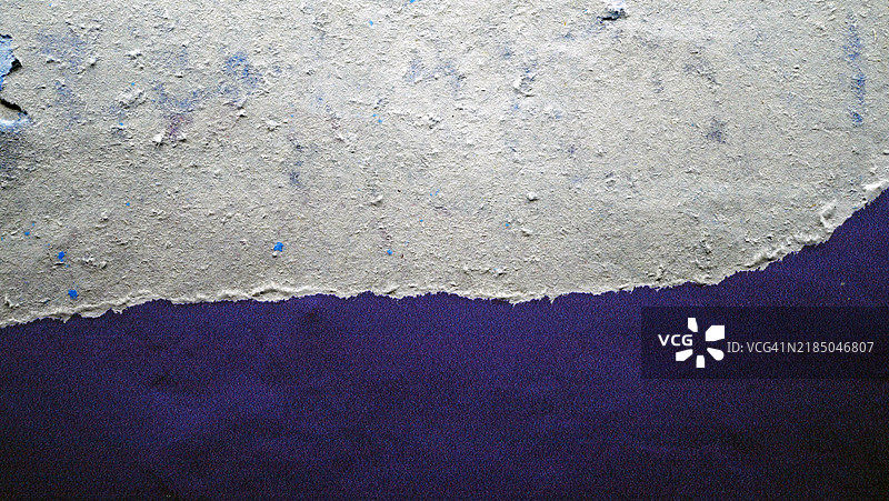 深蓝色海报,粘贴在肮脏的灰色墙壁上,破损不堪。粗糙的纹理。阳光与阴影。经过修饰的照片。图片素材