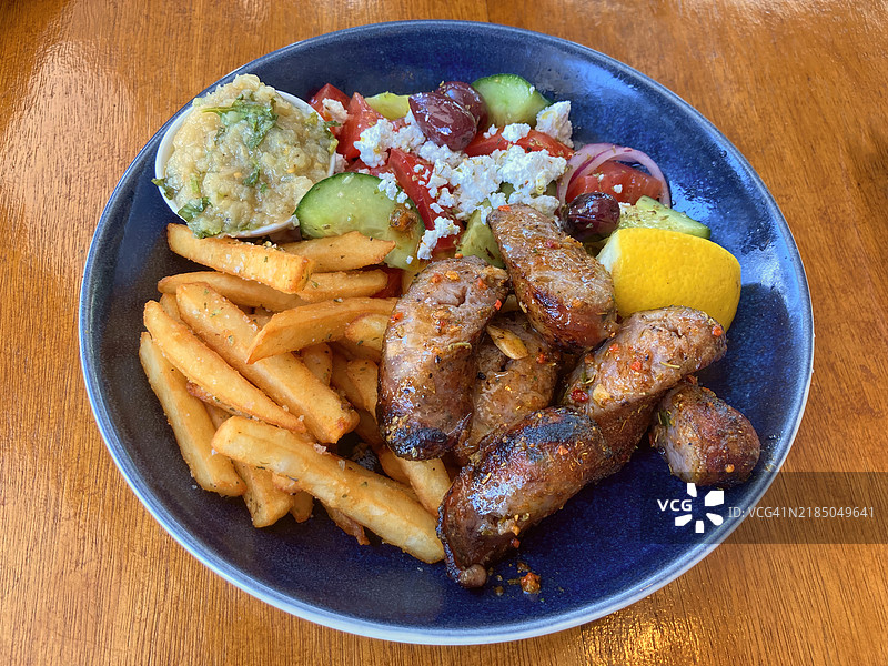 碗里装有调味的炭烤希腊香肠；希腊沙拉；撒有牛至和盐的薯条；以及烟熏茄子酱。图片素材
