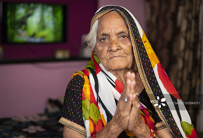 一位年长的印度女性面向镜头，做出合十礼的姿势。图片素材