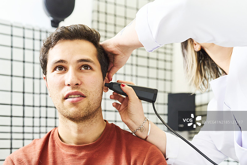 年轻男子坐在女验光师的办公室里，正面朝向镜头进行耳朵的听力检查。图片素材