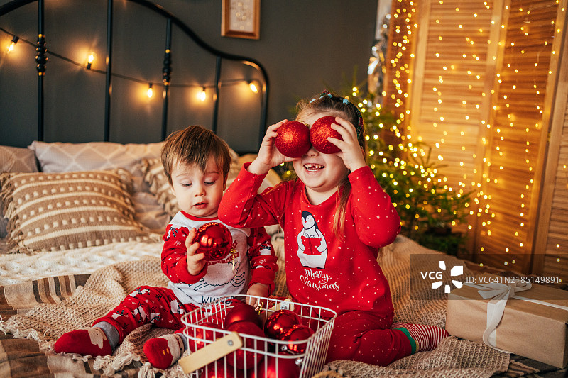 带着人工耳蜗的女孩与她的小弟弟一起玩红色圣诞球图片素材