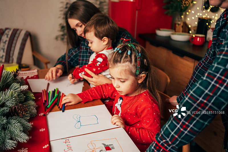 一个戴着人工耳蜗的女孩和家人一起坐在温馨的家中，围坐在桌子旁写信给圣诞老人。图片素材
