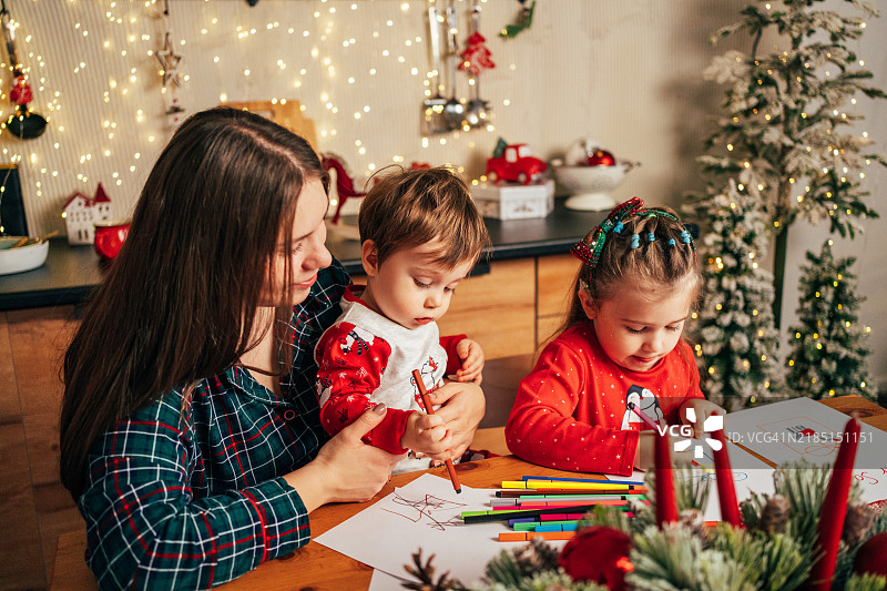 一个戴着人工耳蜗的女孩和家人一起坐在温馨的家中，在桌子上给圣诞老人写信。图片素材