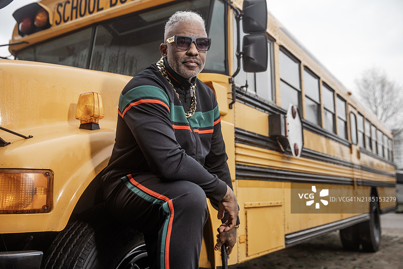1980年代风格的帅气黑人男子，手持音响，身旁有一辆校车图片素材