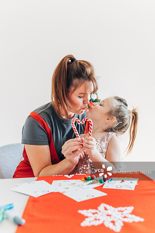 快乐的家庭，母女相拥，手中捧着用糖果手杖做成的心形，互相亲吻庆祝圣诞节。图片素材
