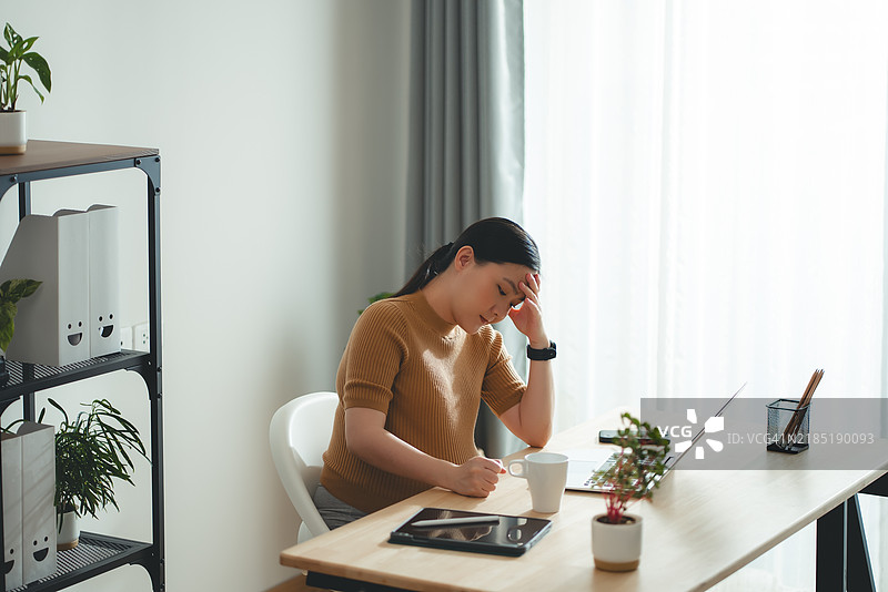 亚洲孕妇坐在家庭办公室，感到担忧，思考工作。图片素材