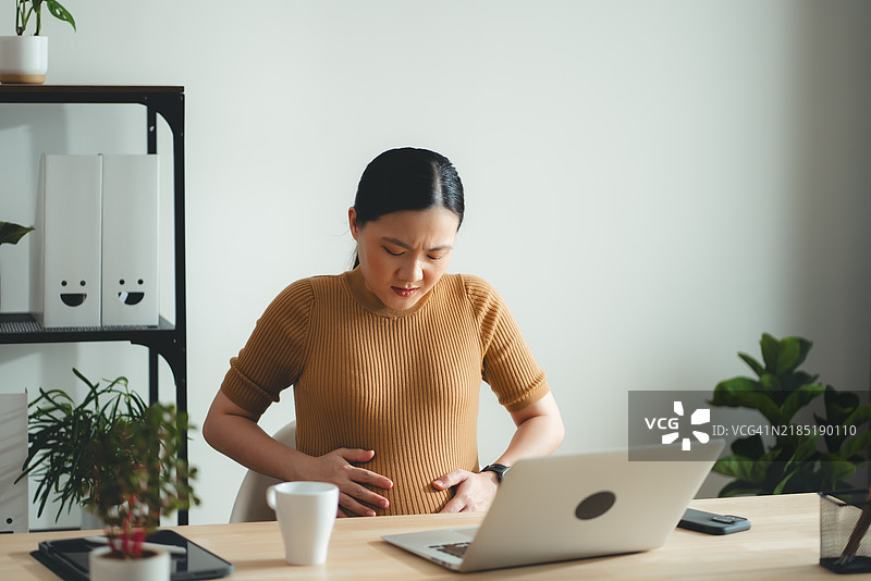 亚洲孕妇在家办公时感到腹痛。图片素材