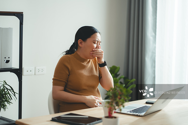 亚洲孕妇在家办公时因晨吐感到不适。图片素材