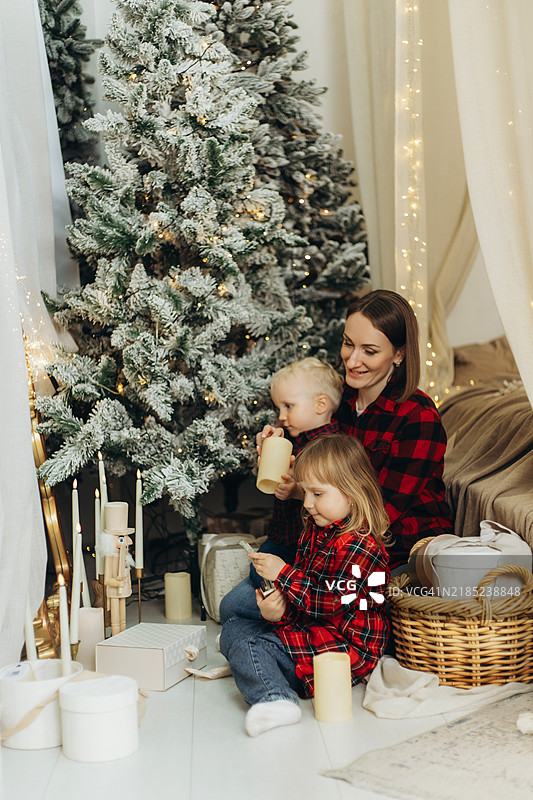 年轻女性和她的小孩们在圣诞树旁庆祝新年，周围有礼物盒。图片素材