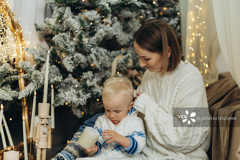 关心的母亲为在新年房间里玩蜡烛的男孩戴上帽子。图片素材