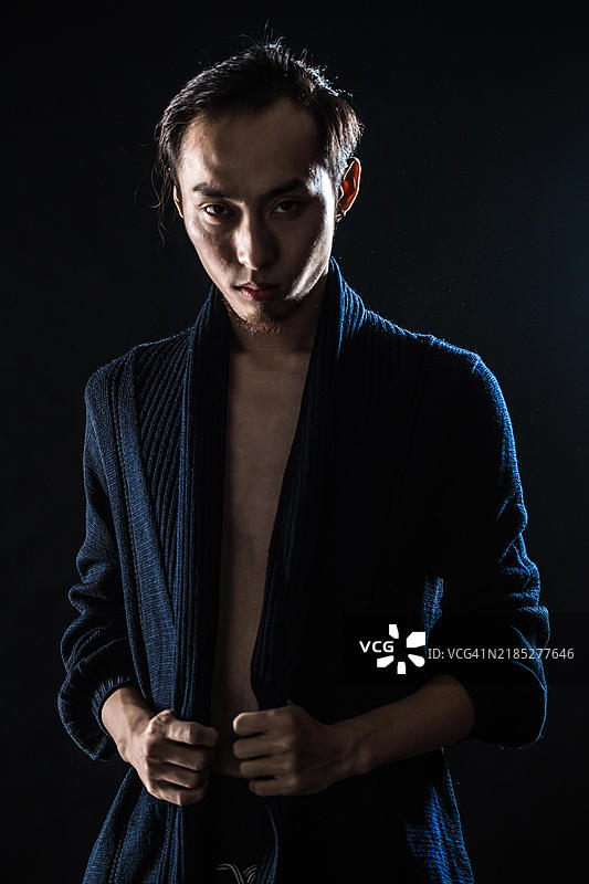 穿着蓝色毛衣的亚洲男性模特，背景为黑色图片素材
