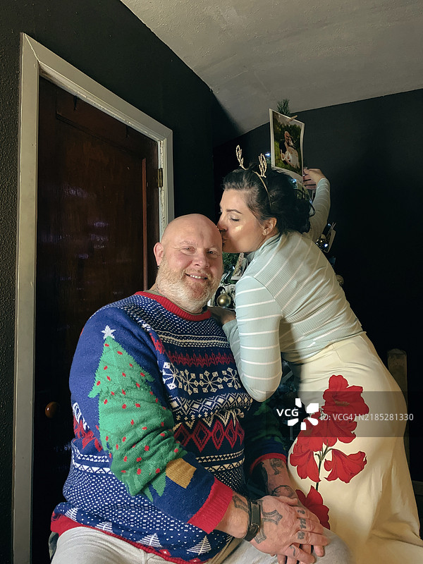 一位早发性阿尔茨海默病患者与他的妻子/照顾者在圣诞树旁快乐地相处。图片素材